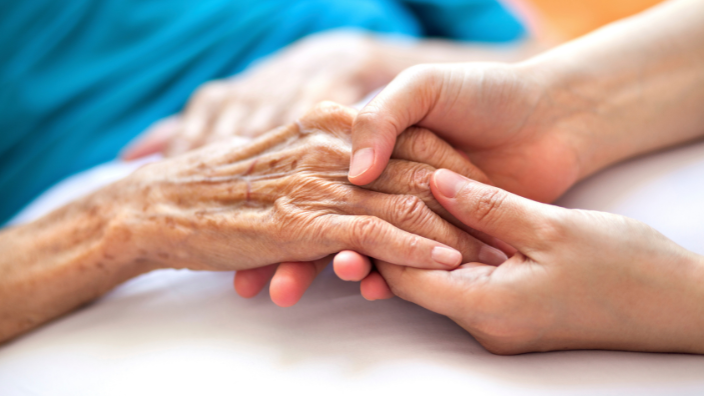 An image of a hand of an elderly client being held between two other hands, in support.