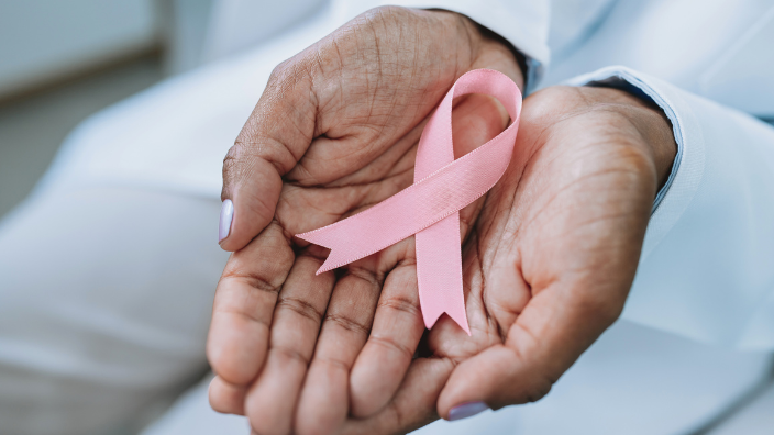 An image of two hands holding a pink ribbon in the shape of the breast cancer symbol.
