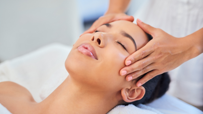 A close-up image of a woman's serene face as she receives a scalp massage by a massage therapist.