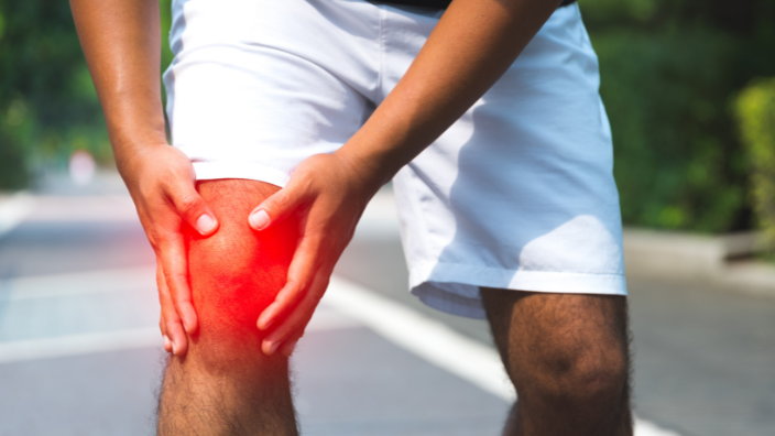 a close-up image of someone holding their knee, it is highlighted red to show it is in pain.